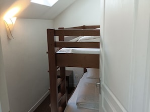 Quarto com beliche, uma secretária pequena e uma porta.