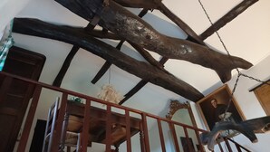 Une pièce avec des poutres apparentes, une rambarde en bois et un luminaire suspendu.