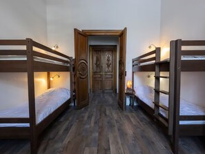 Una habitación con literas, una puerta de madera y una pequeña mesa con lámpara.