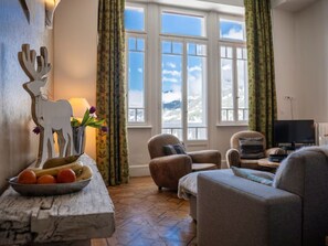 Una sala de estar con vista a las montañas, una mesa de madera con fruta y dos sillones.