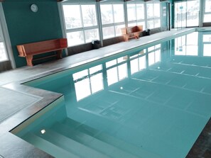 Una piscina interna con acqua cristallina, una panchina in legno sul bordo e ampie finestre che garantiscono luce naturale.