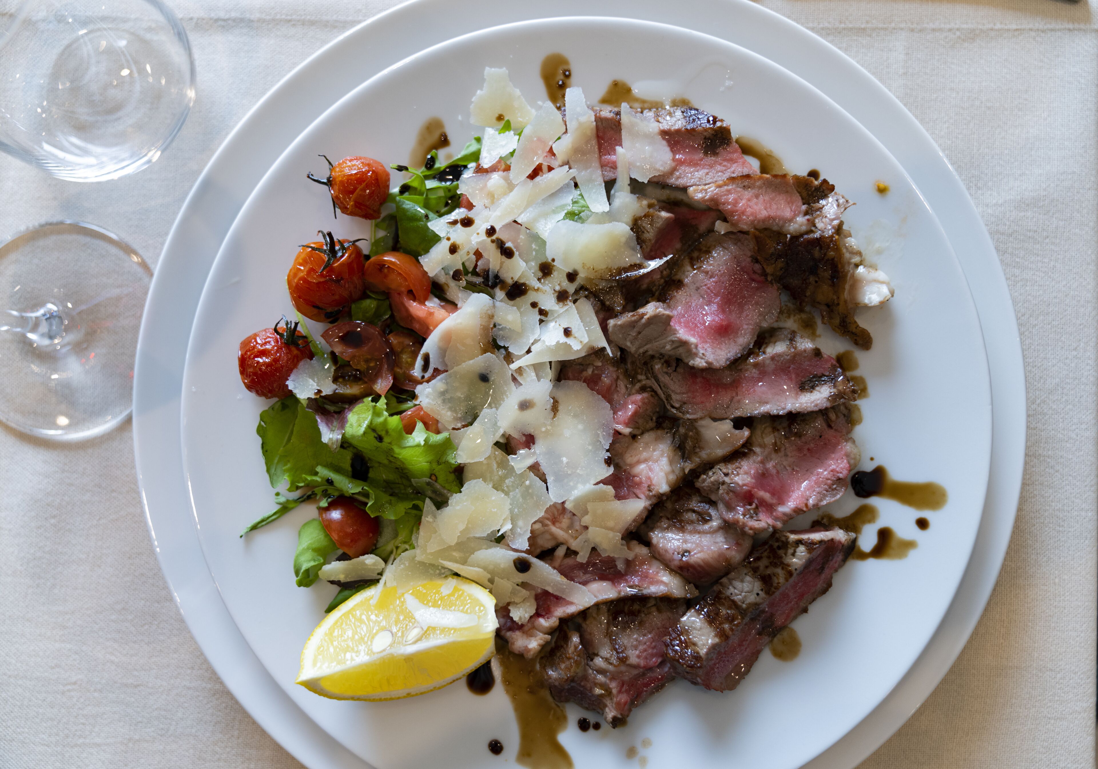 Un plato de comida con carne cortada, verduras y un gajo de limón.