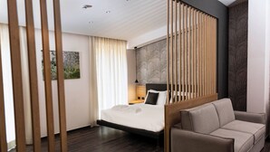 A modern hotel room with a bed, a sofa, a wooden partition, and a wall with a leaf pattern. - Hotel Donna Vì (Geraci Siculo)