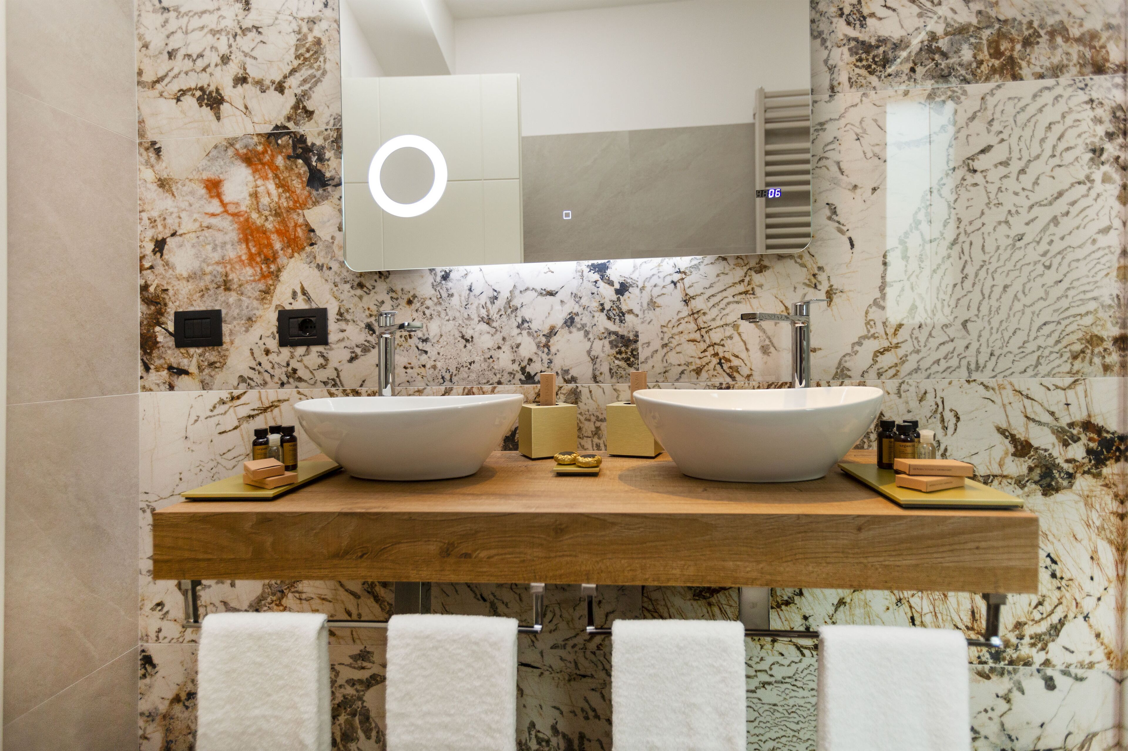 Un baño con dos lavamanos grandes de color blanco, una encimera de madera, paredes de mármol y un espejo sobre los lavamanos.