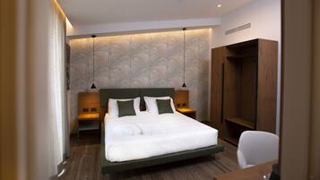 Une chambre d’hôtel moderne avec un grand lit, une tête de lit en bois, deux tables de chevet, une armoire et un bureau avec une chaise.