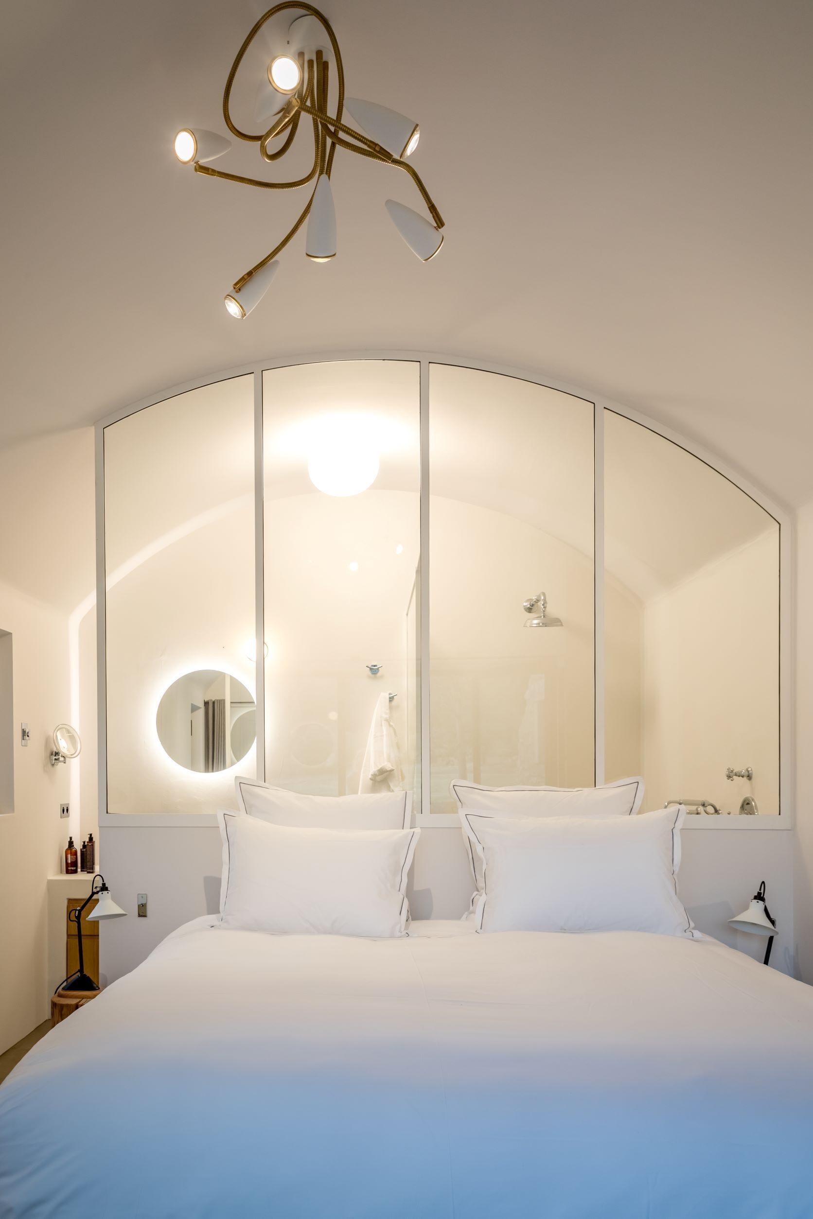 Une chambre d’hôtel moderne avec un grand lit, un miroir incurvé et un luminaire au plafond au design original.