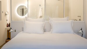 Une chambre d’hôtel moderne avec un grand lit, un miroir incurvé et un luminaire au plafond au design original.