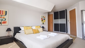 Ein modernes Schlafzimmer mit einem großen Bett, einem Schiebetürenschrank und abstrakter Wandkunst.
