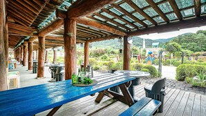 An outdoor wooden deck with a blue table and benches, surrounded by wooden pillars and a glass ceiling. - Gapyeong Acimpunggeongpension (Gapyeong)