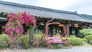 A traditional wooden building with a tiled roof, a swing chair, and vibrant pink flowers in the foreground. - Gapyeong Acimpunggeongpension (Gapyeong)