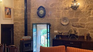 A rustic room with a stone wall, a fireplace, a wooden table with a lamp, and a door leading outside. - A Casa da Ita (OURENSE)