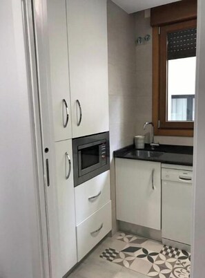 Une cuisine compacte avec des meubles blancs, un four à micro-ondes encastré, un évier et un carrelage décoratif.