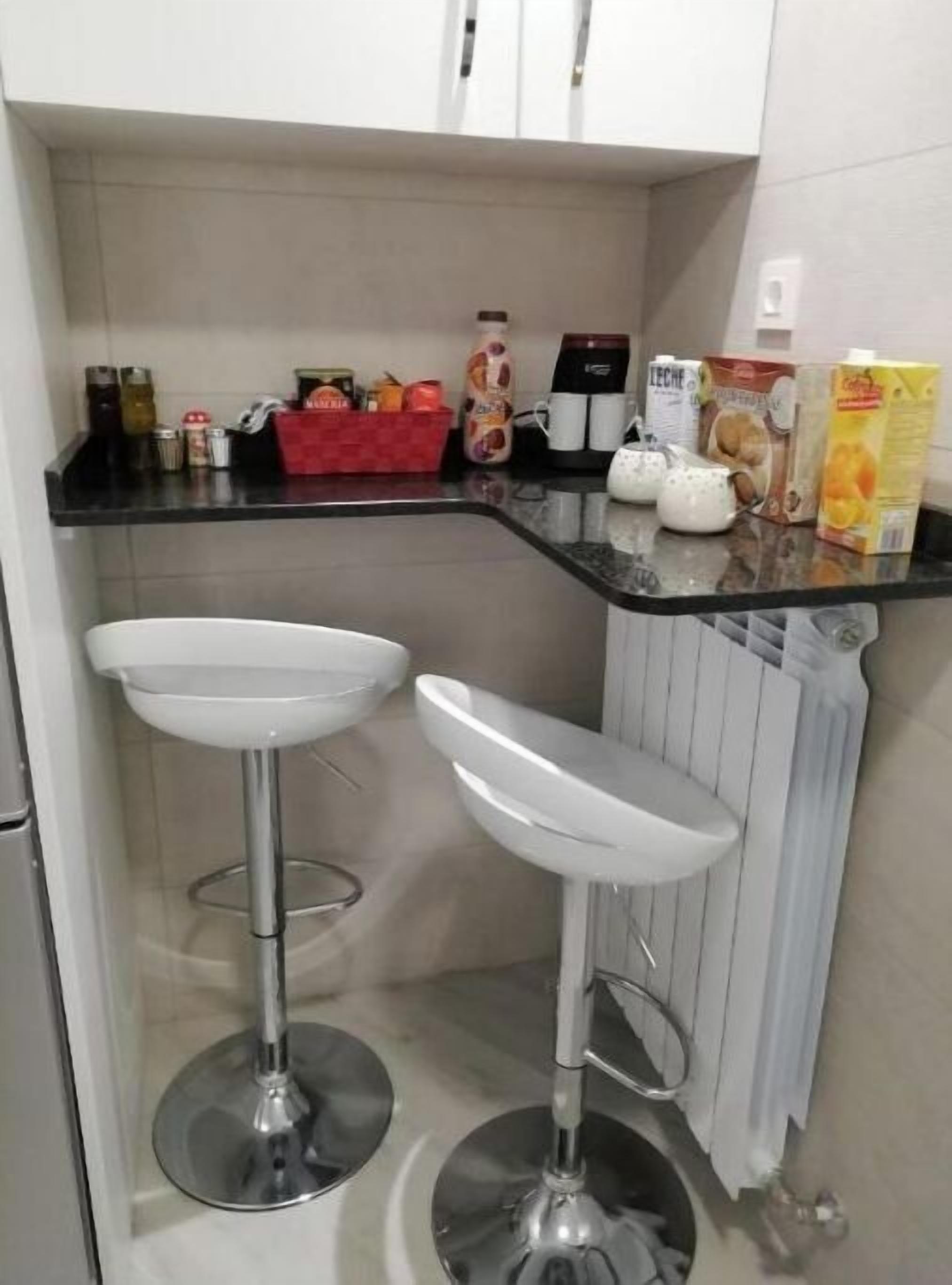 A kitchen with two white bar stools, a black countertop, and various kitchen items.