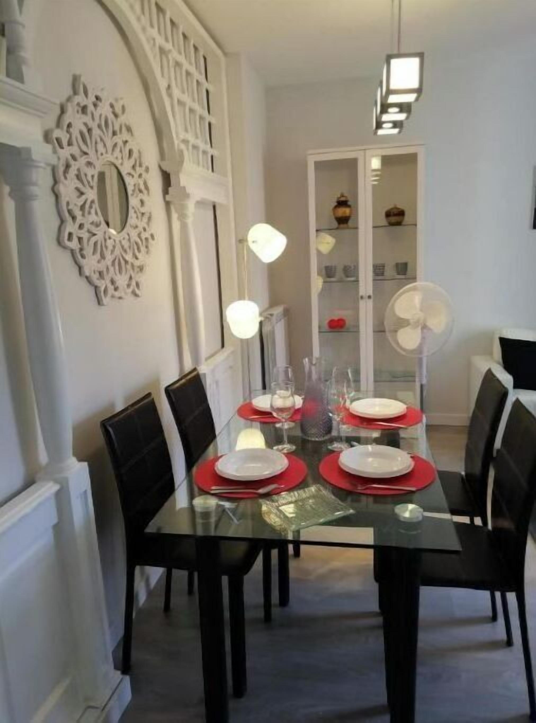 A dining area with a glass table set for four, black chairs, and a white decorative wall piece.