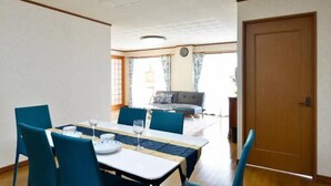 A dining area with a table set for two, a sofa in the background, and a wooden door. - Wing Mihama Beach (Chatan)