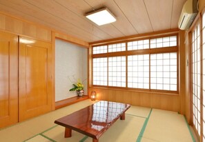 Une pièce traditionnelle japonaise avec un sol recouvert de tatamis, une basse table en bois, des portes coulissantes et une grande fenêtre ornée de panneaux shoji.