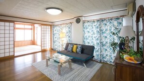 A traditional Japanese room with tatami flooring, a low wooden table, a sofa with cushions, and a decorative cabinet. - Wing Mihama Beach (Chatan)