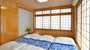 A traditional Japanese-style room with tatami flooring, a futon bed, sliding doors, and a large shoji screen window. - Wing Mihama Beach (Chatan)