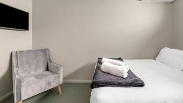Ein Hotelzimmer mit grauem Sessel, einem Bett mit weißer und grauer Bettwäsche sowie einer Klimaanlage an der Wand.