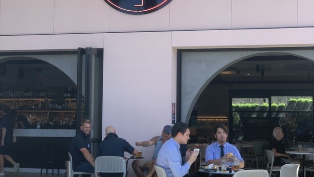 An outdoor seating area with tables and chairs, a neon flamingo sign above, and a bar visible through the entrance. - Illinois Hotel (Five Dock)