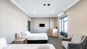 A hotel room with two beds, a flat-screen TV, a desk, a chair, and a window with blinds. - Illinois Hotel (Five Dock)