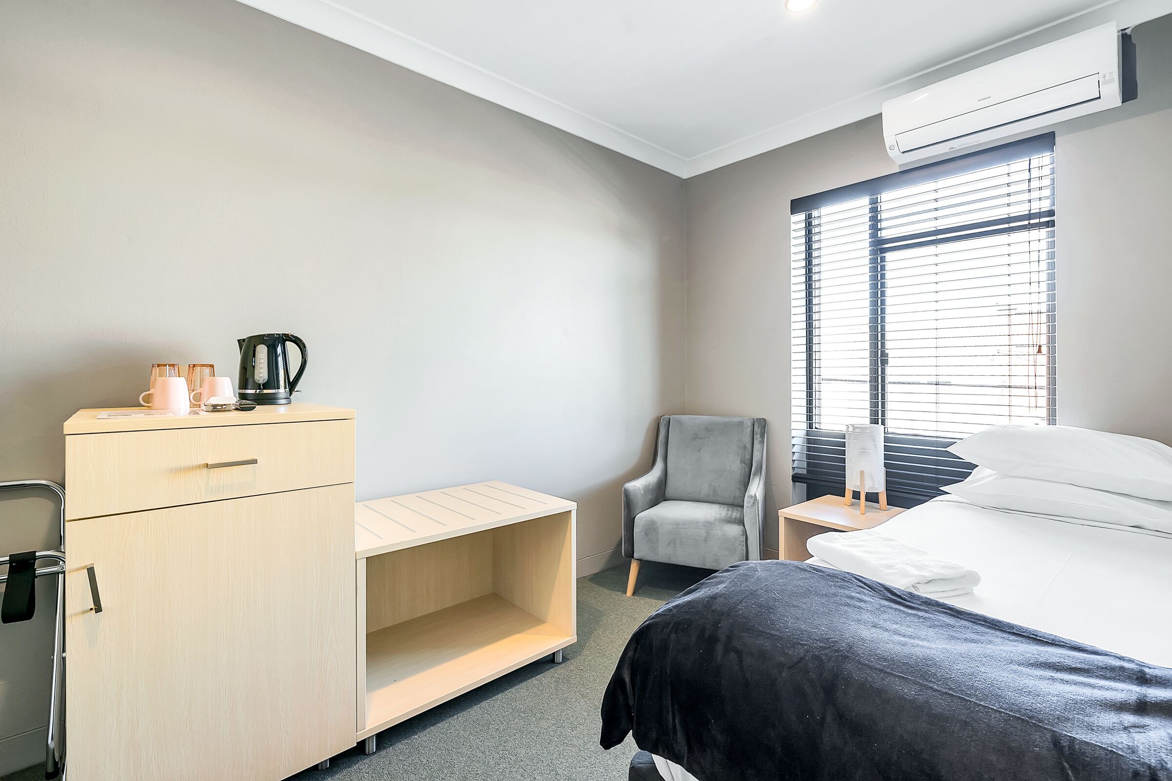 A hotel room with a bed, a desk, a chair, a wardrobe, and a window with blinds.