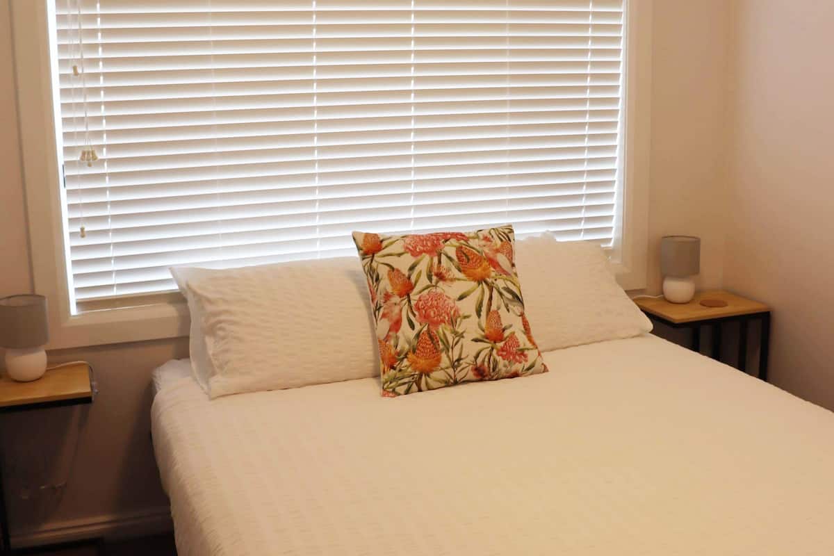Una cama bien hecha con un cojín estampado y dos mesitas de noche con lámparas.