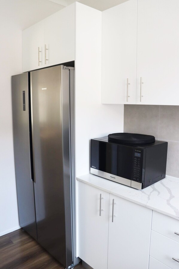 Una cocina con armarios blancos, un refrigerador de acero inoxidable y un microondas negro sobre una encimera de mármol.