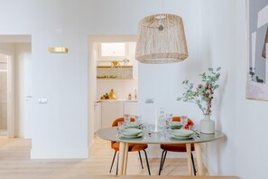 Ein zeitgemäßer Essbereich mit einem runden Tisch für vier Personen, einer hängenden gewobenen Leuchte und einem Blumentopf an der Wand.