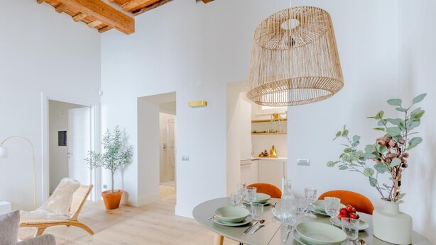 A dining area with a round table set for four, a wicker pendant light, and potted plants. - Casa Lazzaro Contemporary Ground Floor Apartment (Lucca)