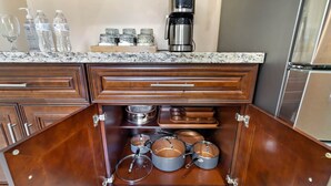 A kitchen with wooden cabinets, a coffee maker, and various pots and pans stored inside.