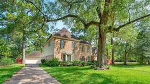 A two-story house with a brick exterior, a front porch, and a driveway leading to a garage.