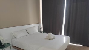 Un lit bien fait, avec du linge de lit blanc, une table de chevet avec une lampe, et une vue sur un rideau sombre.