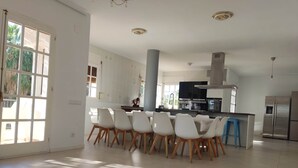 Une cuisine spacieuse dotée d’appareils électroménagers modernes, un coin repas avec des chaises blanches et de grandes fenêtres laissant entrer la lumière naturelle.