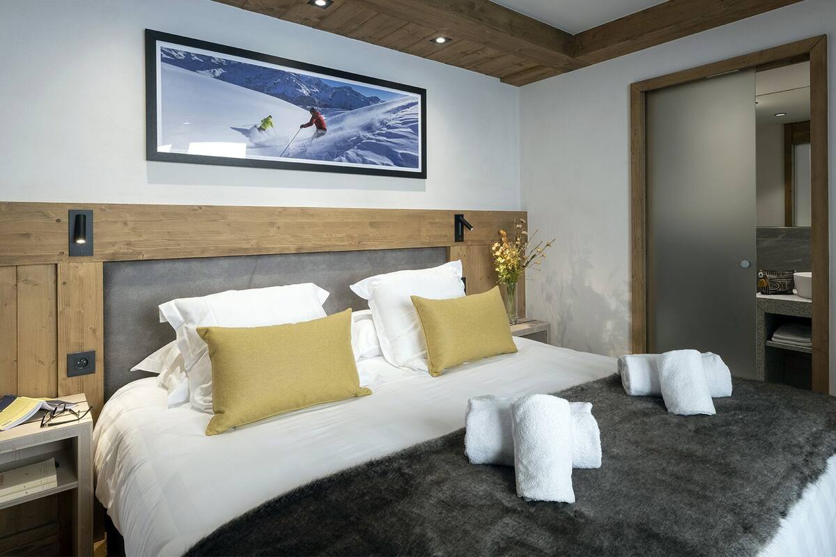 A hotel room with a large bed, wooden headboard, a framed picture of skiers, and a mirror.