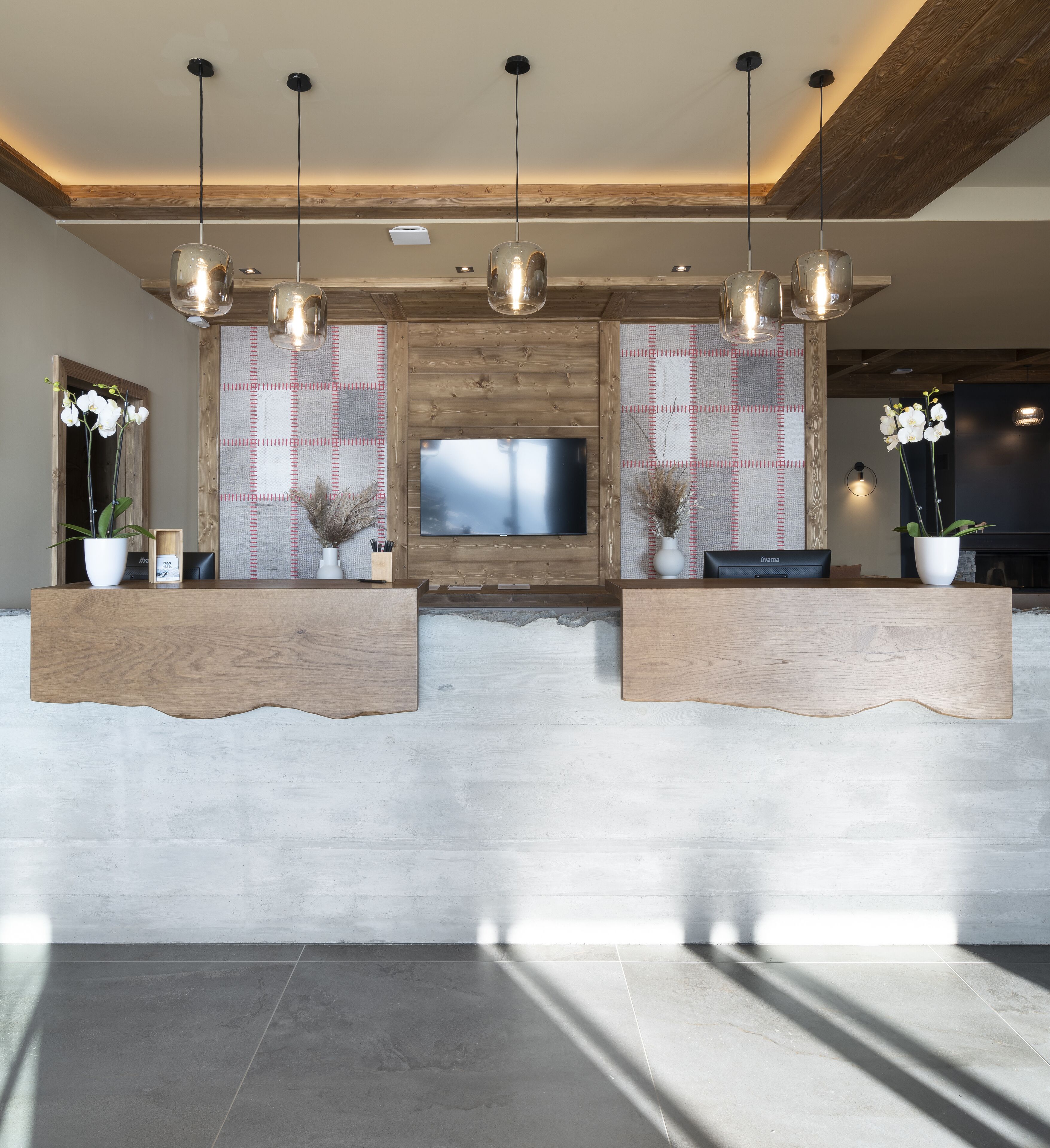 A reception area with wooden reception desks, a flat-screen TV, and pendant lighting.