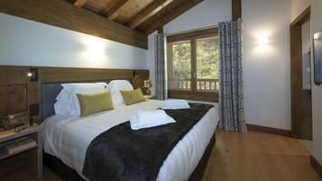 A bedroom with a wooden headboard, a large window with a view of trees, and a bed with white linens and a dark throw.