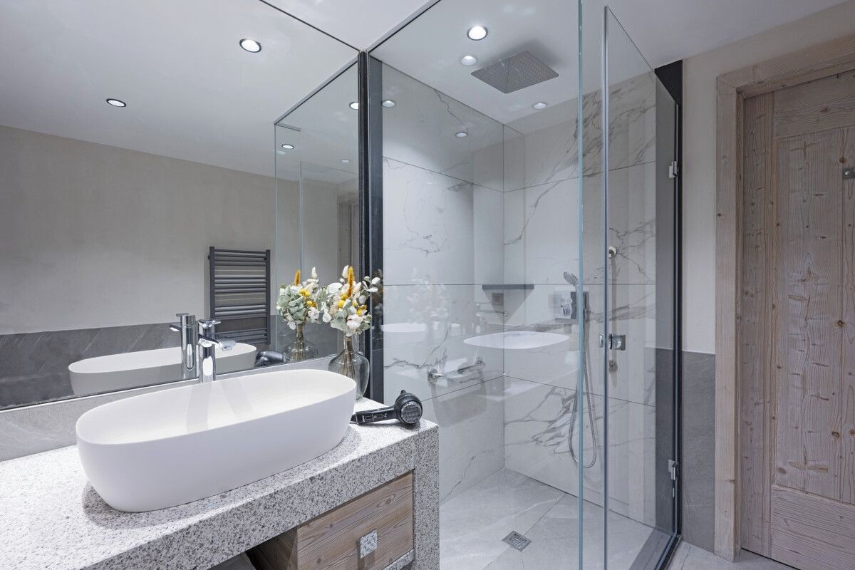 A modern bathroom with a large white sink, a glass shower enclosure, and a wooden door.