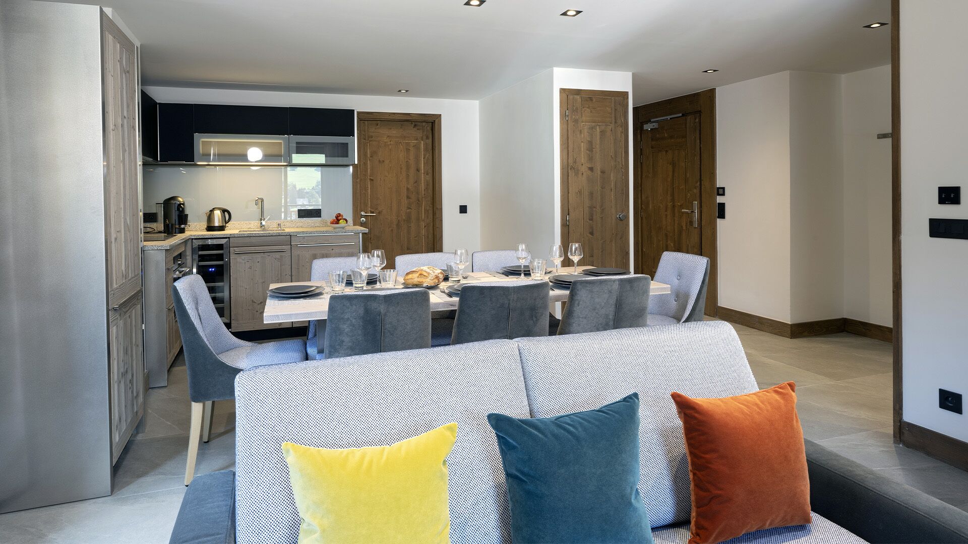 A modern dining area with a table set for four, surrounded by grey upholstered chairs.