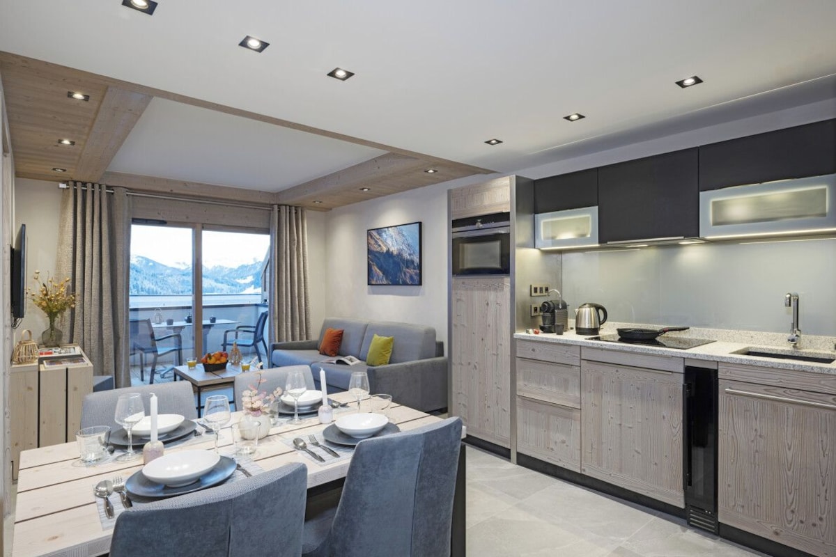 A modern kitchen with built-in appliances, a dining area with a table set for four, and a view of the mountains through large windows.