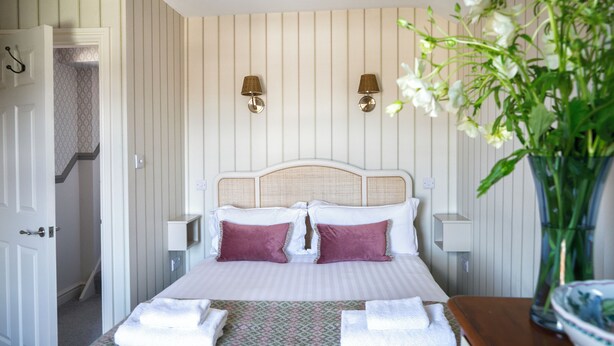 A neatly made bed with two pillows, a bedside table with a vase of flowers, and a wall-mounted lamp. - Deluxe 2 bedroom upper floor apartment (Harrogate)