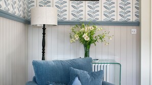 A room with a blue armchair, a lamp, a framed deer picture, and a vase with flowers on a glass table. - Deluxe 2 bedroom upper floor apartment (Harrogate)