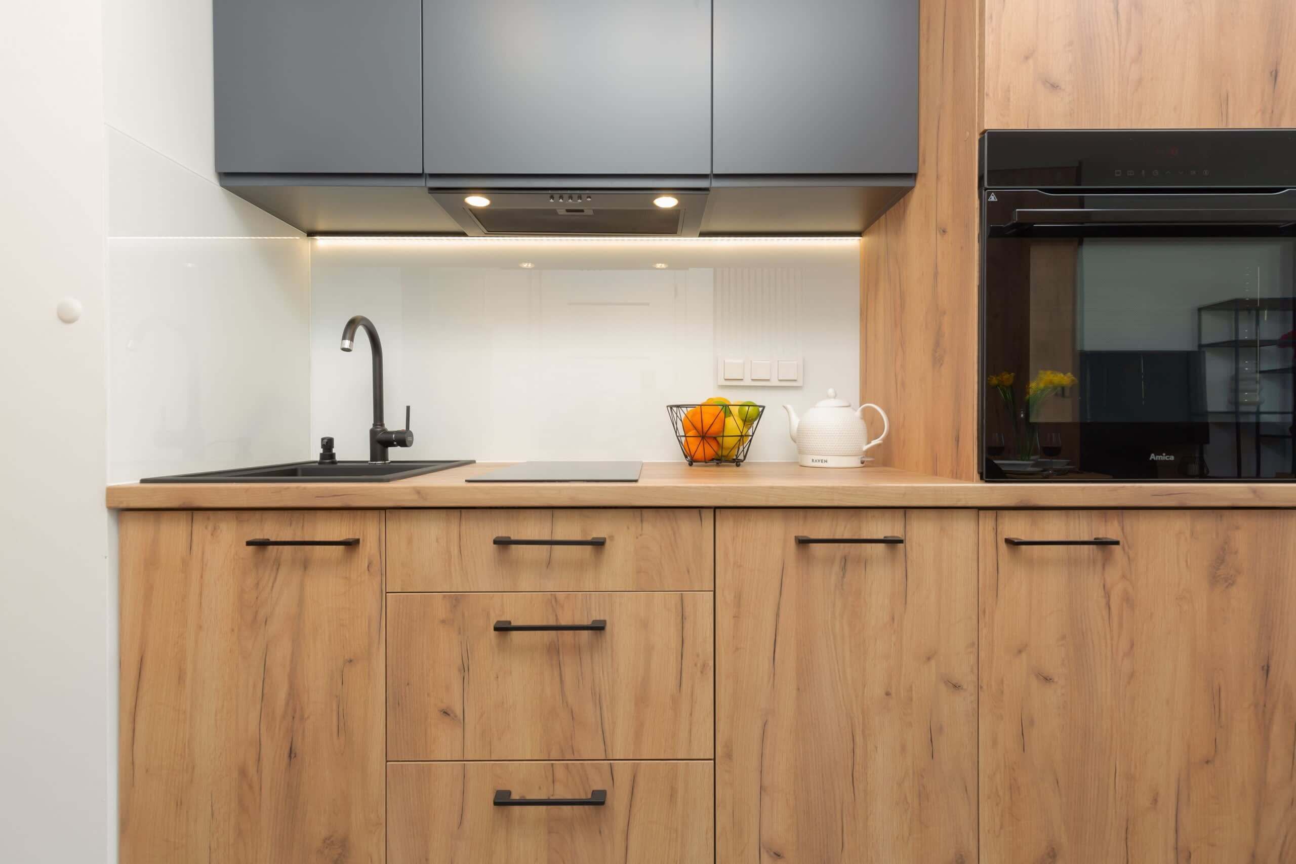 Una cucina moderna con mobili in legno, un rubinetto nero, un bollitore e una ciotola di frutta.