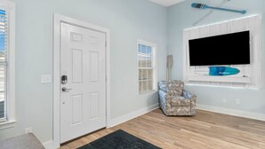 Una stanza con una porta bianca, una poltrona con motivo decorativo, una TV a parete e una decorazione a tema surf.