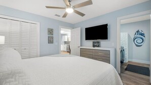 Una camera da letto con un letto, una ventola a soffitto, una TV e un comò.