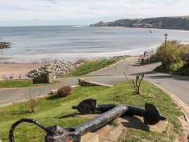 Un parque costero con una gran escultura de ancla, un muro de piedra y un camino que lleva a la playa.