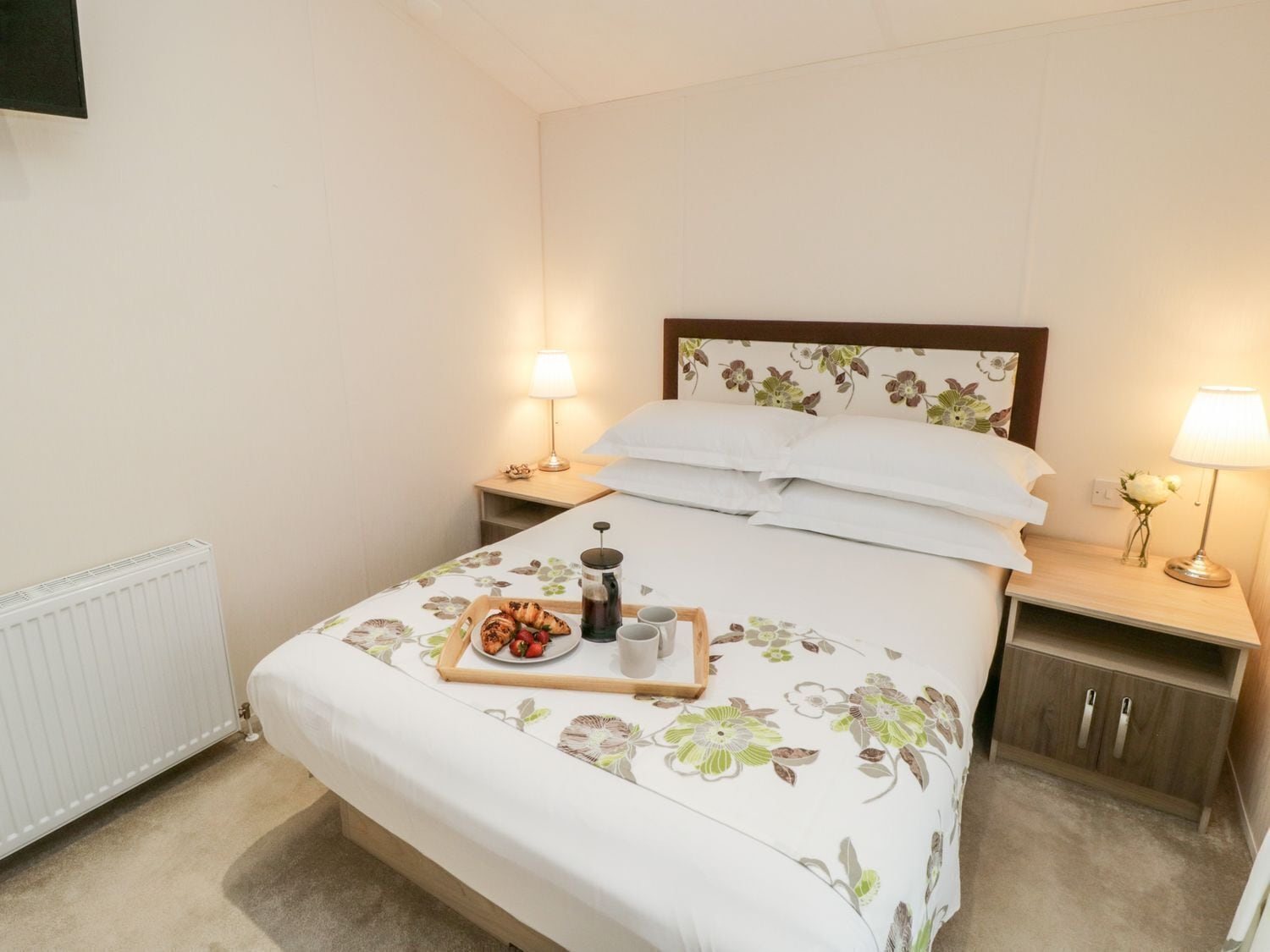A neatly made bed with a floral bedspread, a tray with food and drinks, and bedside lamps.
