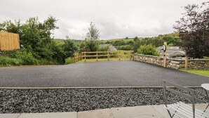 Un espace de stationnement dallé, agrémenté d’une barrière en bois, d’un mur en pierre et d’un banc.