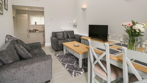 Un salon moderne avec un canapé gris, une table à manger en bois et un téléviseur.