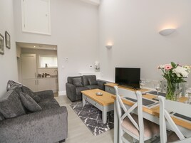 A modern living room with a grey sofa, a wooden dining table, and a TV.